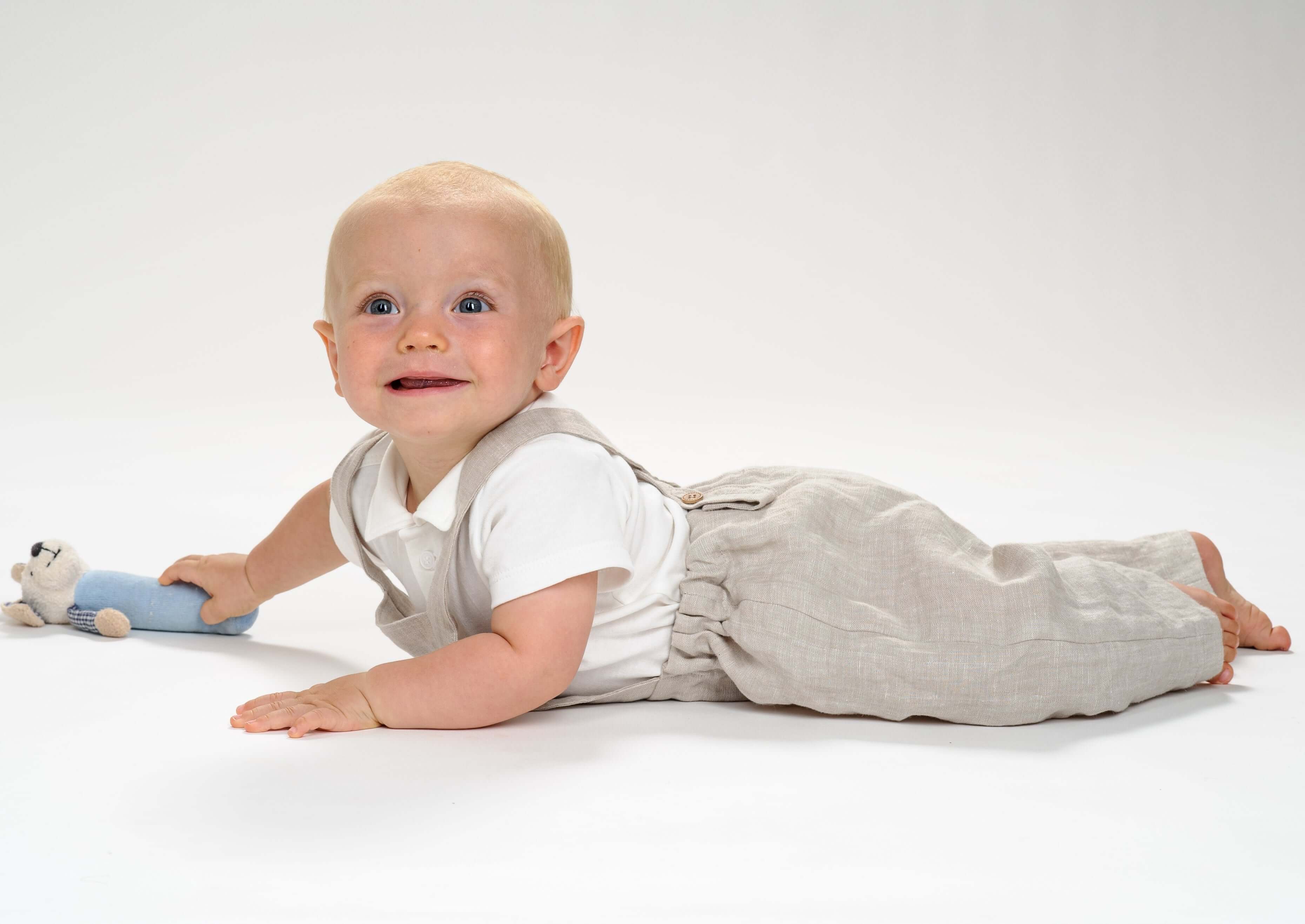 Baby in Schnittmuster Latzhose MAX lächelt im Liegen mit Spielzeug.