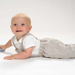 Baby in Schnittmuster Latzhose MAX lächelt im Liegen mit Spielzeug.