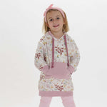 Schnittmuster Tunika Hoodie ARWEN: Mädchen trägt einen floral bedruckten Tunika Hoodie in Rosa.