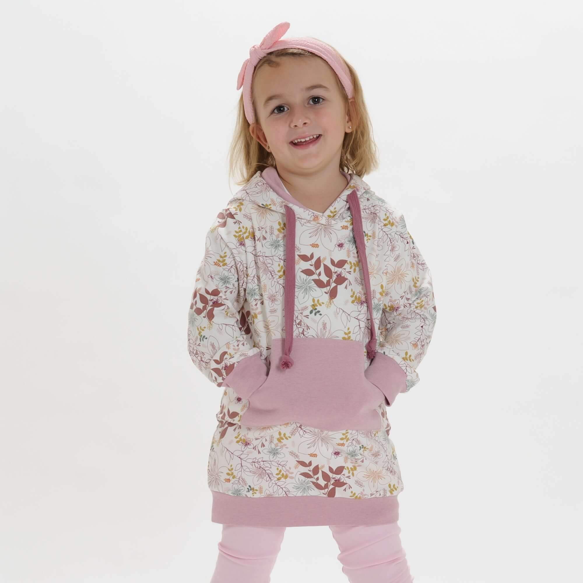 Schnittmuster Tunika Hoodie ARWEN: Mädchen trägt einen floral bedruckten Tunika Hoodie in Rosa.