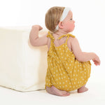 Schnittmuster Baby Overall Jumpsuit – Kleinkind im gelben Overall mit Blumenmuster, sitzt auf einem weißen Würfel.