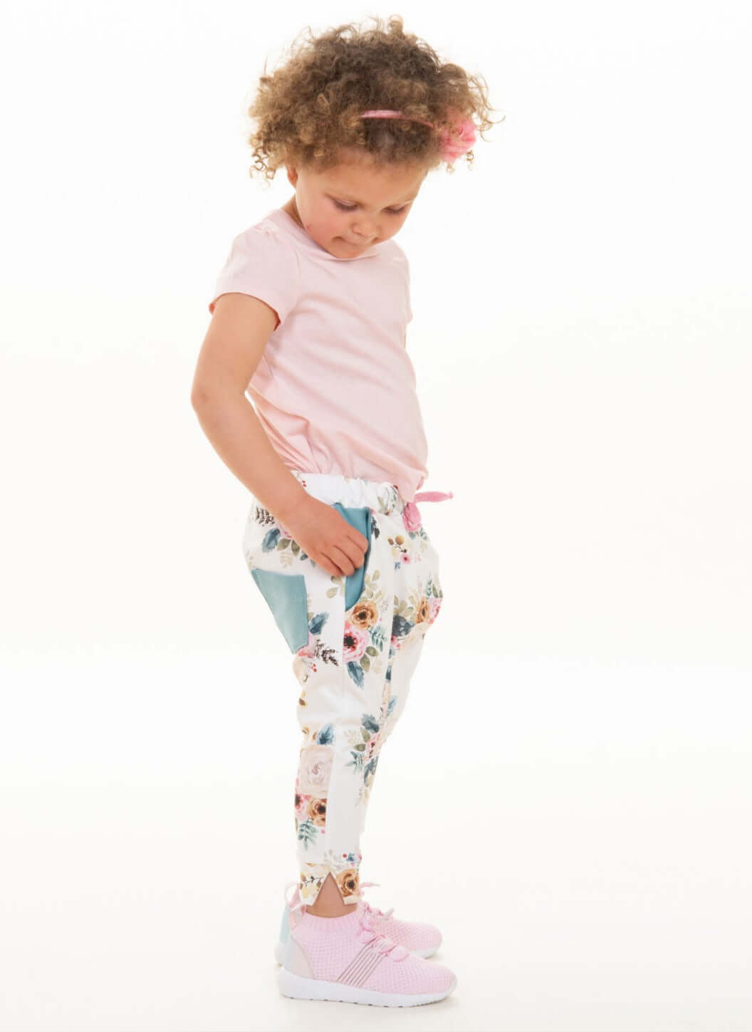 Mädchen in Haremshose mit Blumenmuster, trägt pinkes T-Shirt und Schuhe, zeigt das Schnittmuster Haremshose DADO.