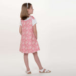 Schnittmuster Schürzenkleid JULE PDF 3-in-1, Mädchen in rosa Pinafore-Kleid mit Blumenmuster.