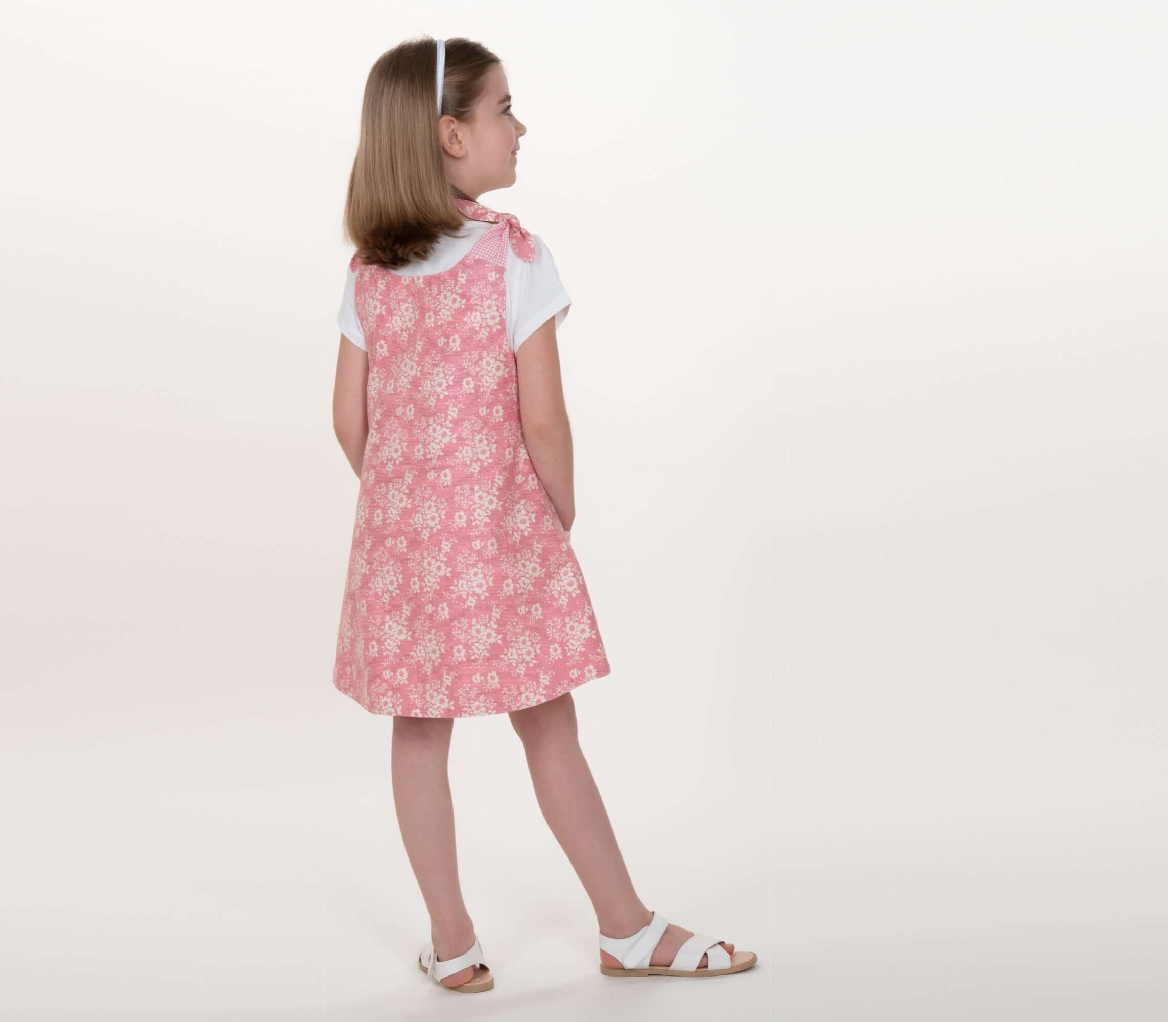 Schnittmuster Schürzenkleid JULE PDF 3-in-1, Mädchen in rosa Pinafore-Kleid mit Blumenmuster.
