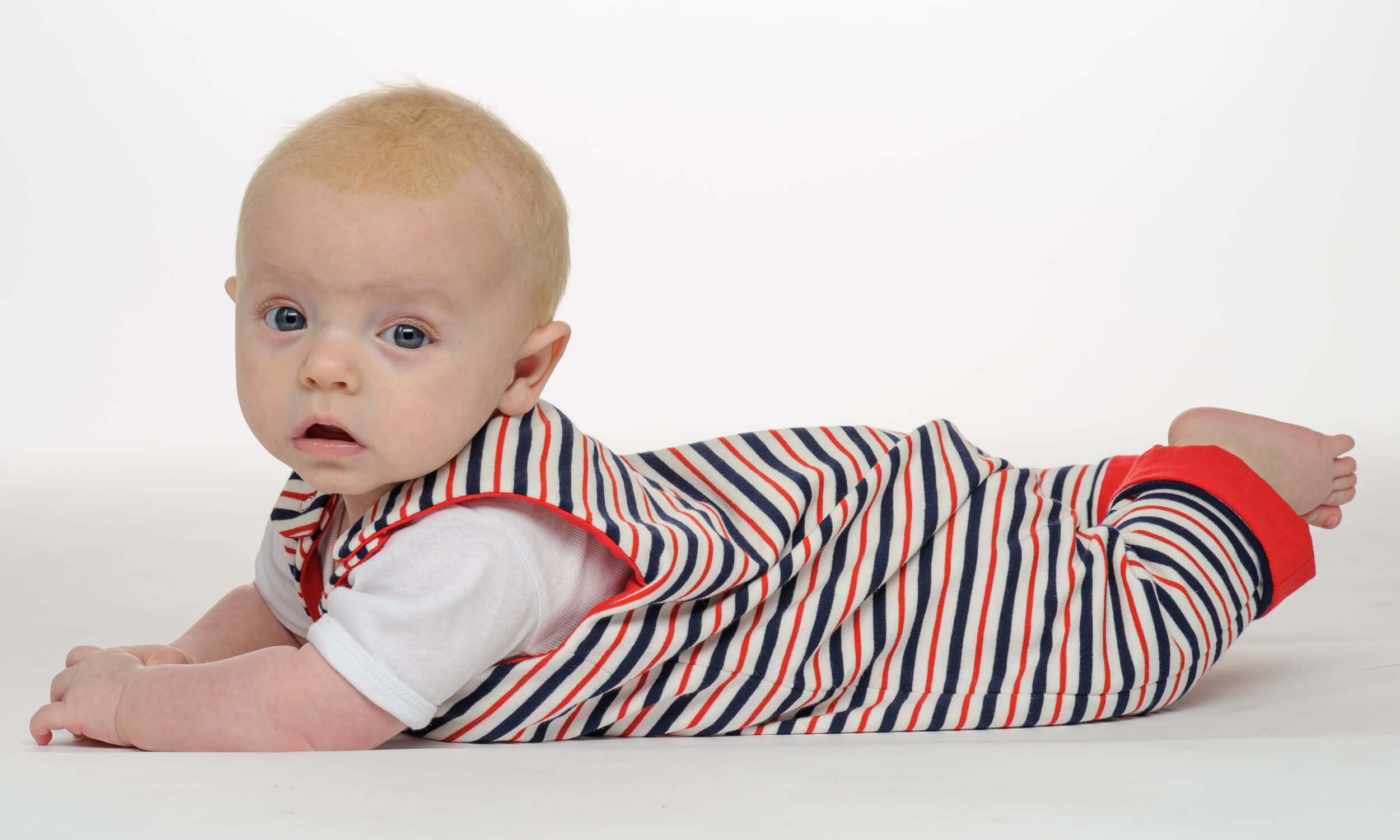 Schnittmuster Strampler LEO - Baby in gestreiftem Strampler liegt auf dem Bauch, süß und bequem.