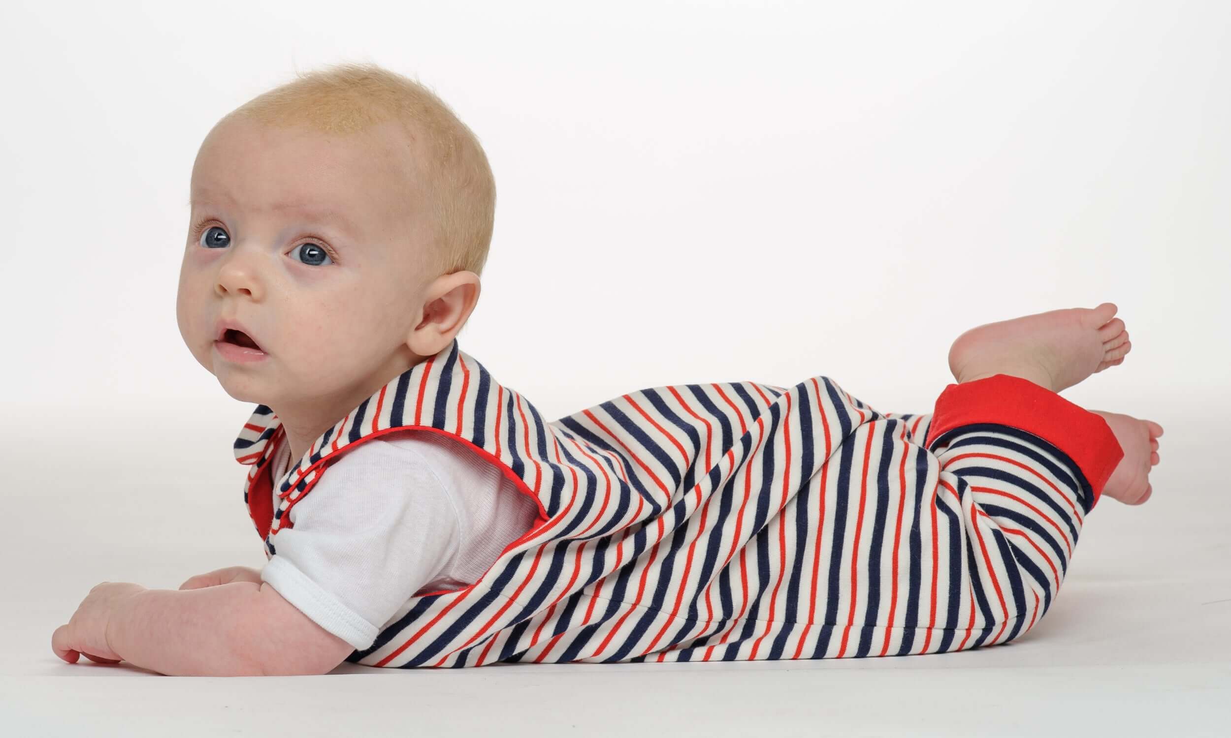 Baby in gestreiftem Strampler liegt auf dem Bauch, trägt das Schnittmuster Strampler LEO.