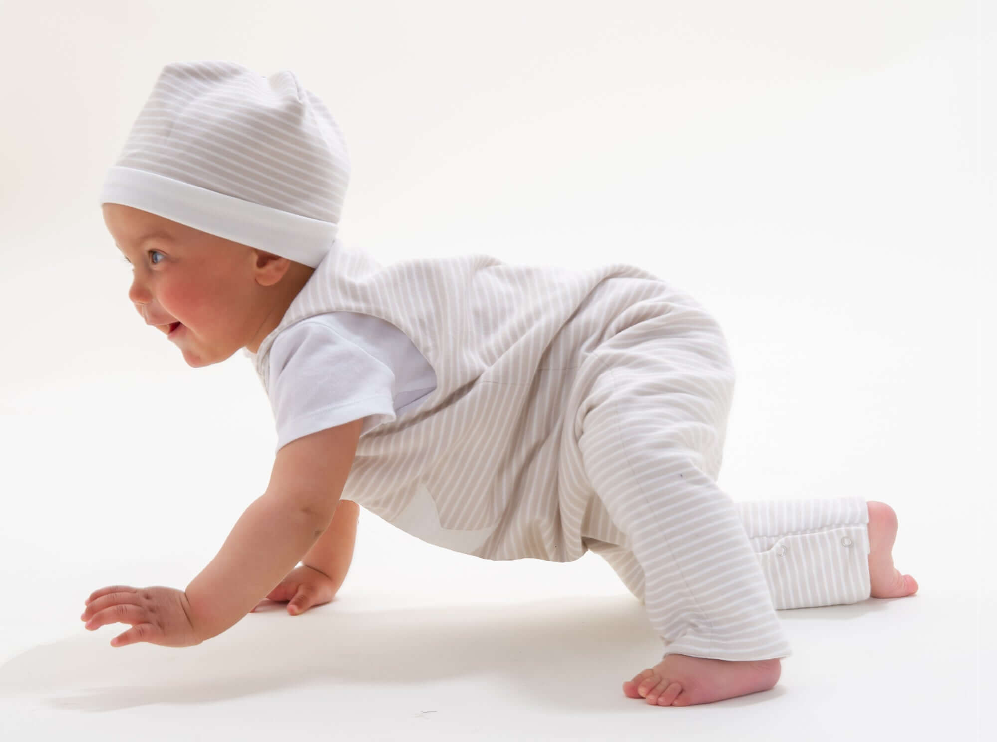 Schnittmuster Set Baby Strampler und Mütze in Verwendung, Baby mit gestreiftem Strampler und Mütze, crawlt spielerisch.