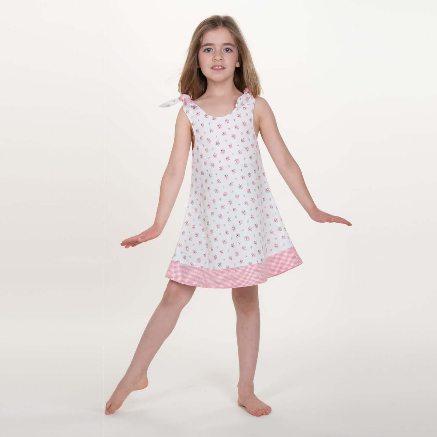 Schnittmuster Schürzenkleid JULE, Mädchen im Pinafore-Stil mit buntem Muster und pinkem Saum, fröhlich posierend.