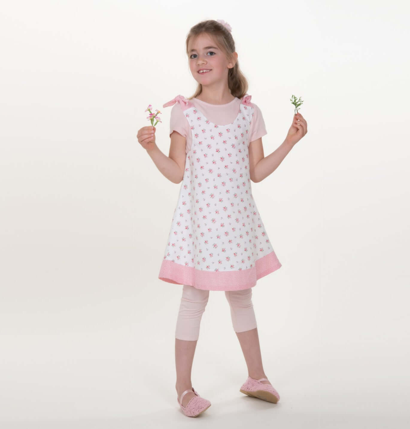 Mädchen trägt ein Schürzenkleid nach dem Schnittmuster Schürzenkleid JULE PDF 3-in-1 mit Blumenmuster.