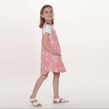 Schnittmuster Schürzenkleid Mädchen trägt ein rosa Schürzenkleid, das nach Schnittmuster Schürzenkleid JULE PDF 3-in-1 genäht wurde.
