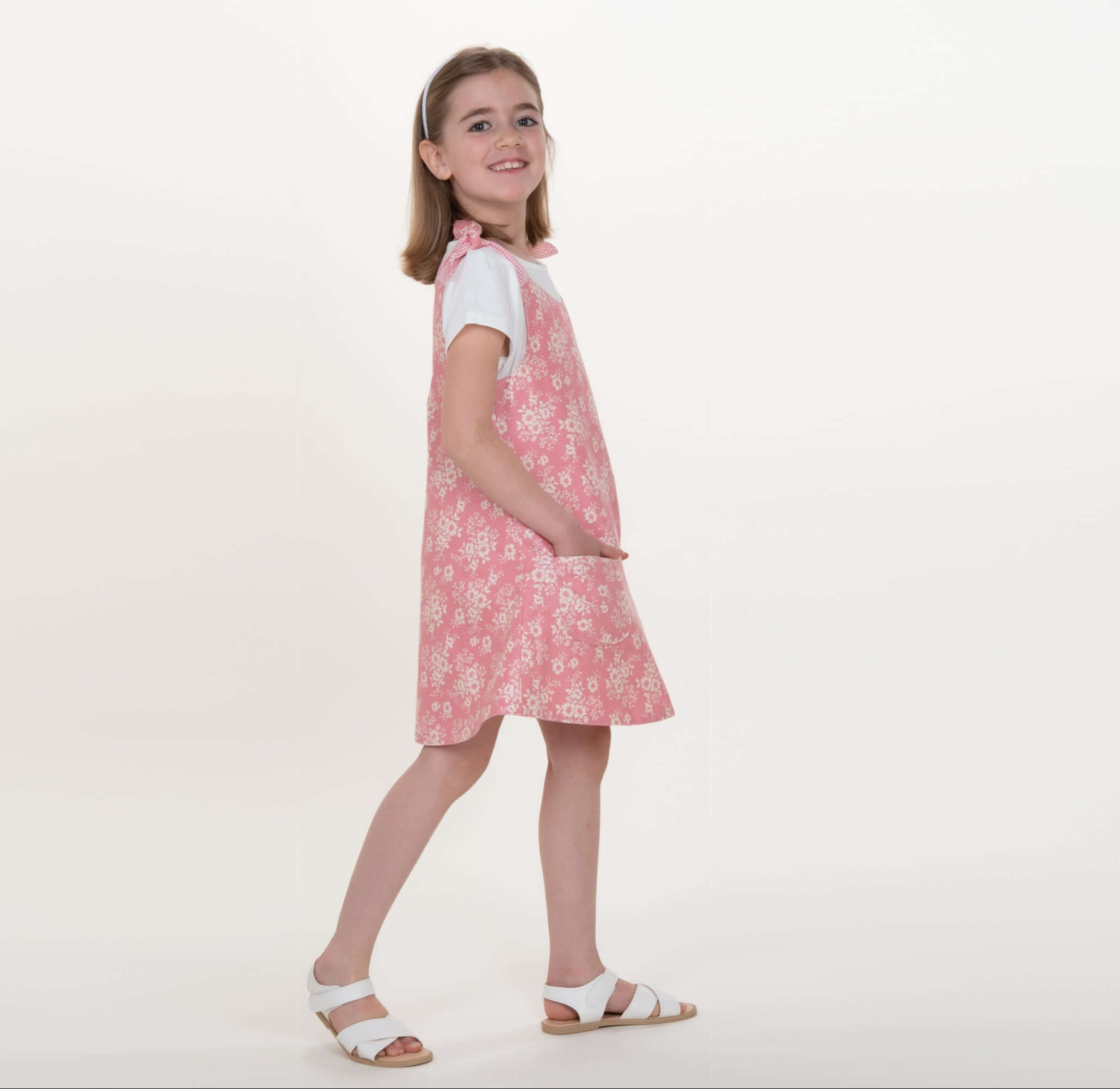 Schnittmuster Schürzenkleid Mädchen trägt ein rosa Schürzenkleid, das nach Schnittmuster Schürzenkleid JULE PDF 3-in-1 genäht wurde.