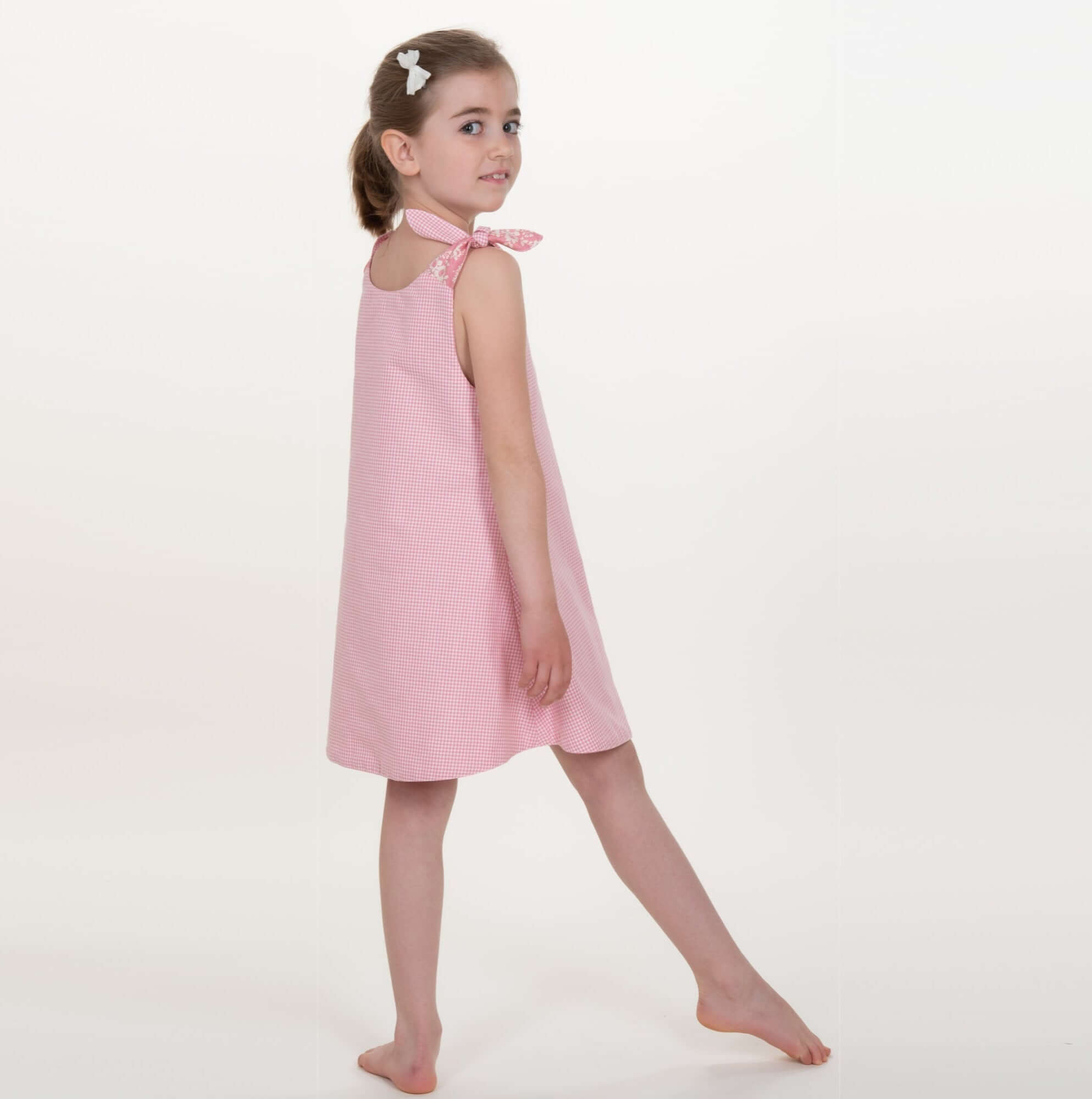 Schnittmuster Schürzenkleid JULE PDF 3-in-1, Mädchen im rosafarbenen Schürzenkleid von hinten.