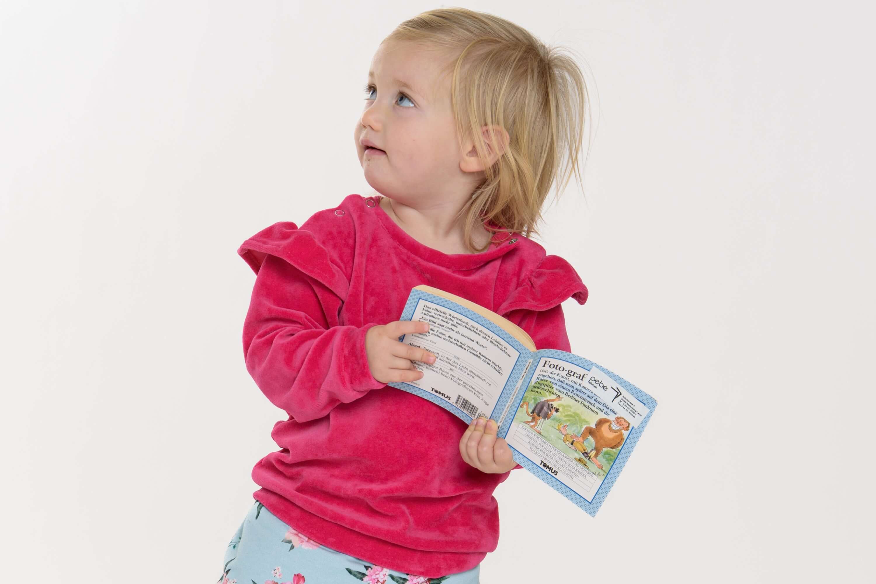 Kleines Mädchen in einem rosa Baby Sweatshirt, das ein Buch liest, passend zum Schnittmuster Baby Sweatshirt.
