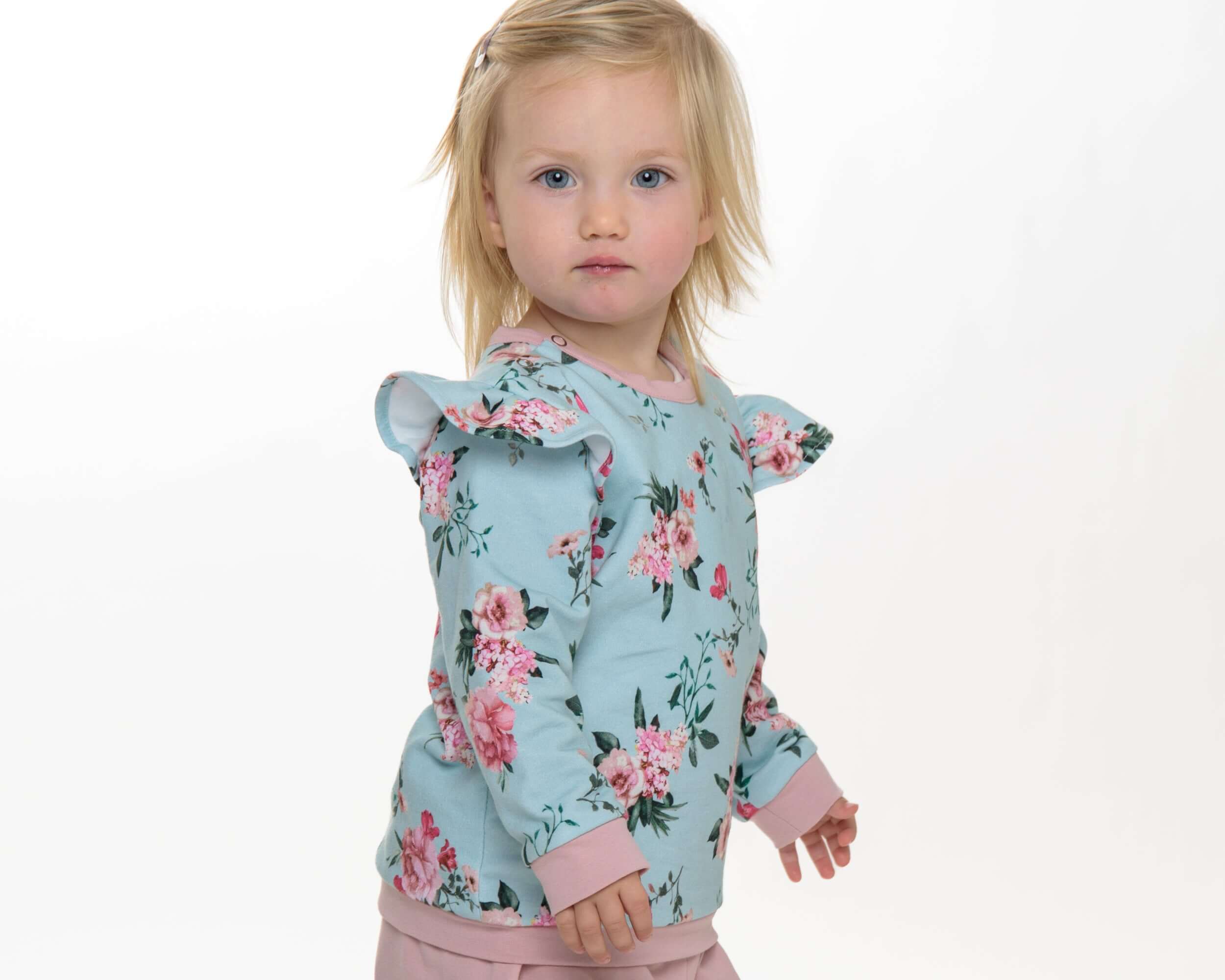 Schnittmuster Baby Sweatshirt mit Rüschen, rosa Blumenmuster und Schulterdruckknöpfen für Mädchen.