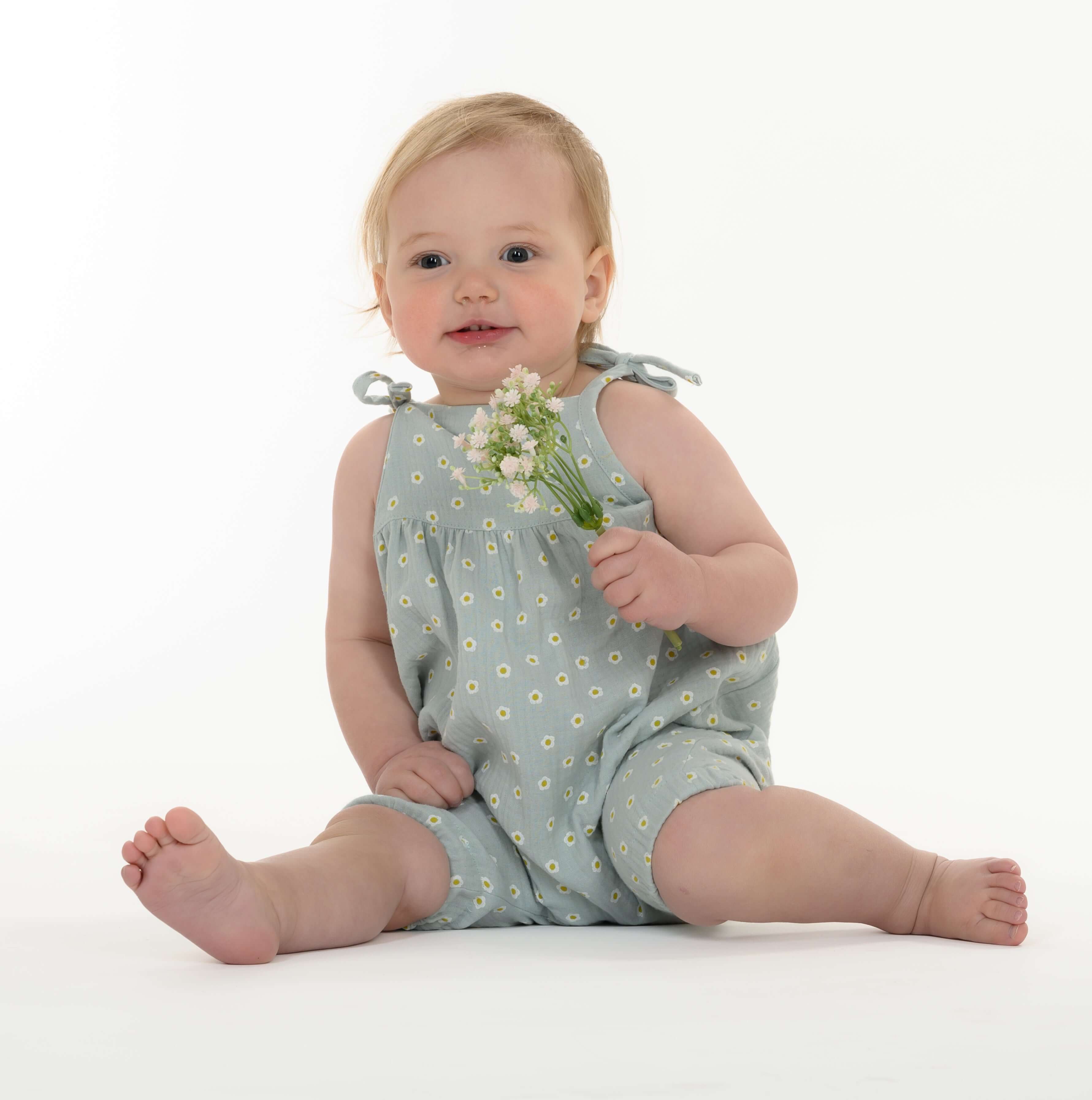 Schnittmuster Baby Overall Jumpsuit NELE – Kleinkind im blauen Overall mit Blumen, sitzend und lächelnd.