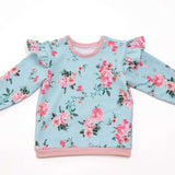 Schnittmuster Baby Sweatshirt mit floralen Mustern, Rüschenärmeln und rosa Details für stilvolle Babykleidung.