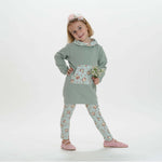 Schnittmuster Mädchen Tunika Hoodie ARWEN in sanftem Grün mit Blumenmuster-Leggings und einer Blume in der Hand.