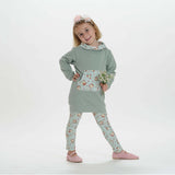 Schnittmuster Mädchen Tunika Hoodie ARWEN in sanftem Grün mit Blumenmuster-Leggings und einer Blume in der Hand.