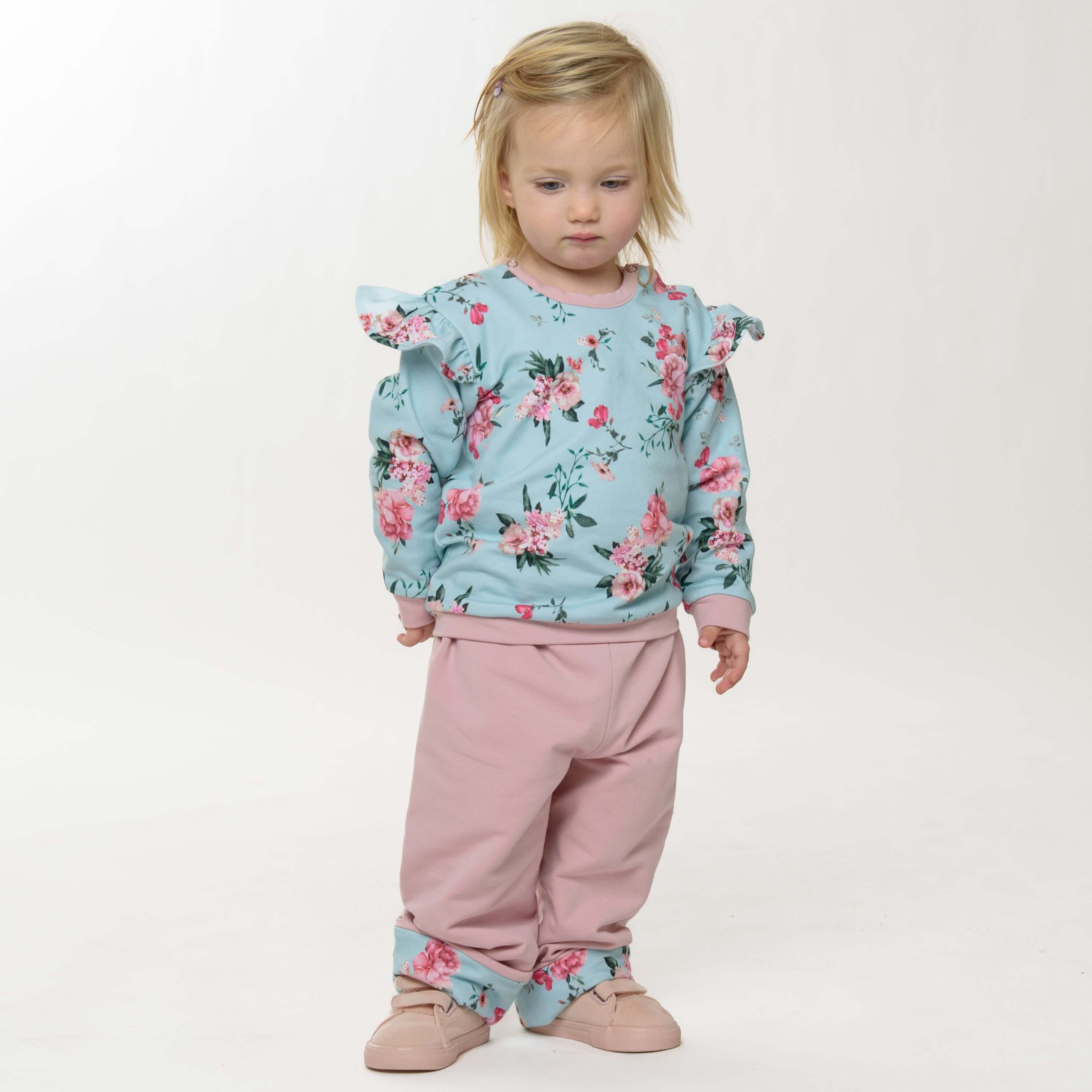 Schnittmuster Baby Sweatshirt in blauer Blüten-Optik, getragen von einem kleinen Mädchen mit rosa Hosen.