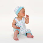 Schnittmuster Baby-Overall & Mütze PDF 2-in-1 Unisex in pastellfarben mit Blumenmuster, Baby sitzt und denkt.