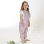 Schnittmuster Latzhose DAISY PDF in rosa für Kinder, Größen 68/74-116/122, mit Rüschen und gekreuzten Trägern.