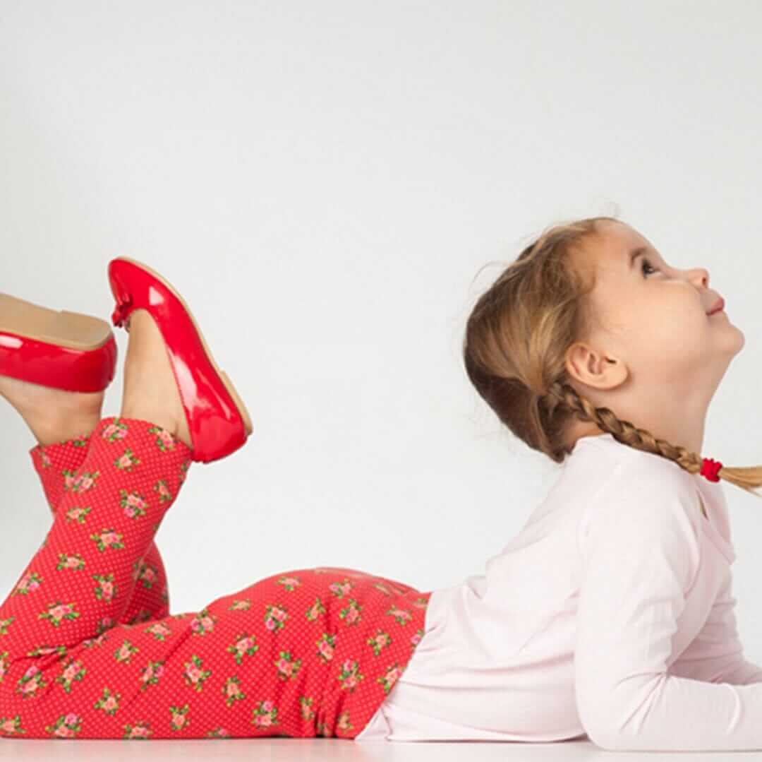 Schnittmuster Baby Kinder Leggings, lächelndes Mädchen mit roten Leggings und Schuhen, auf dem Boden liegend.