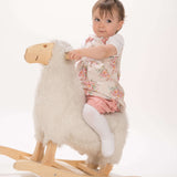 Schnittmuster Baby Twinset Babykleid Hängerchen und Pumphose, Baby auf einem Holz-Schaukel-Schaf mit einem blumigen Kleid.