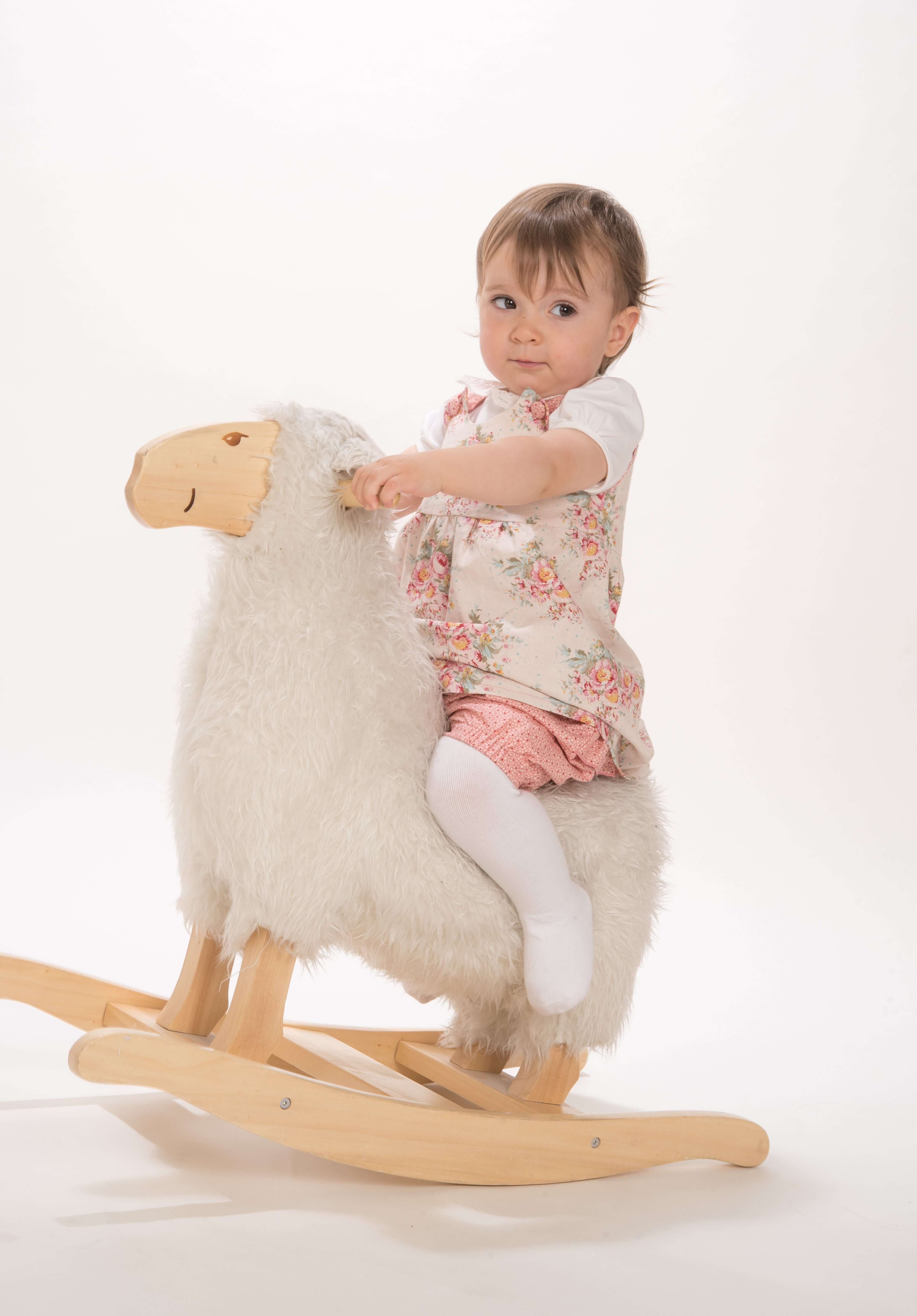 Schnittmuster Baby Twinset Babykleid Hängerchen und Pumphose, Baby auf einem Holz-Schaukel-Schaf mit einem blumigen Kleid.