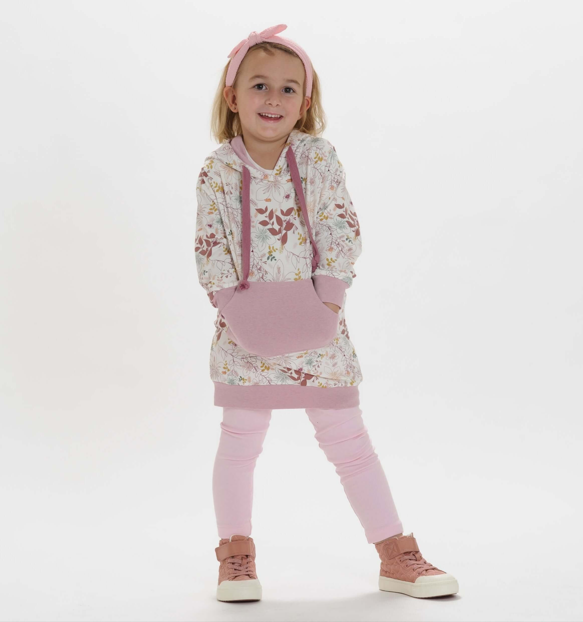 Schnittmuster Tunika, Mädchen in floralem Hoodie mit Kapuze, rosa Leggings und sportlichen Schuhen, modischer Look.